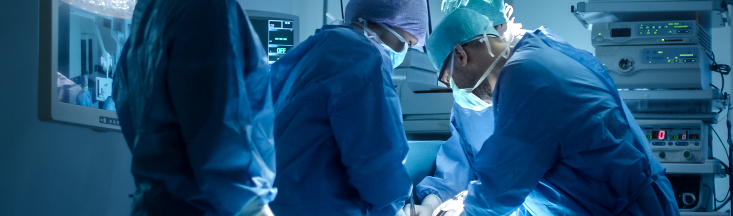 A team of surgeons in blue gowns, surgical caps, and masks focused on performing an operation under a bright surgical light.