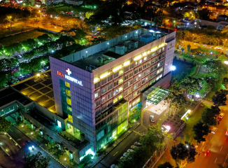 Aerial nighttime view of Eka Hospital lit up with illuminated signage and surrounding city streets with car traffic.