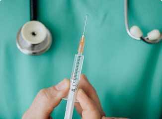 A healthcare professional holding a liquid-filled syringe upright with green scrubs and a stethoscope in the background