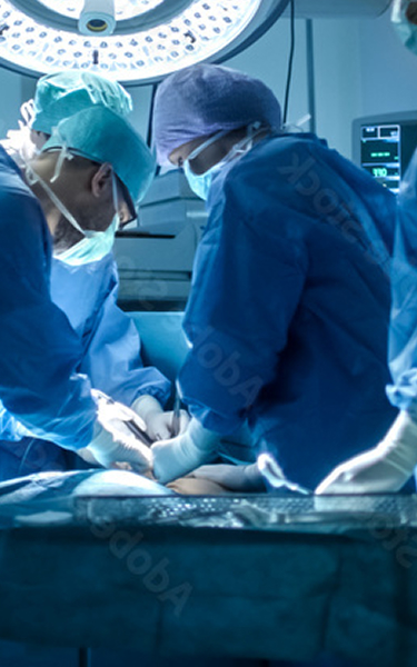 A team of surgeons in blue gowns, surgical caps, and masks focused on performing an operation under a bright surgical light.